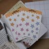 Twee stickervellen met stickers van sterren in het roze, geel en blauw.