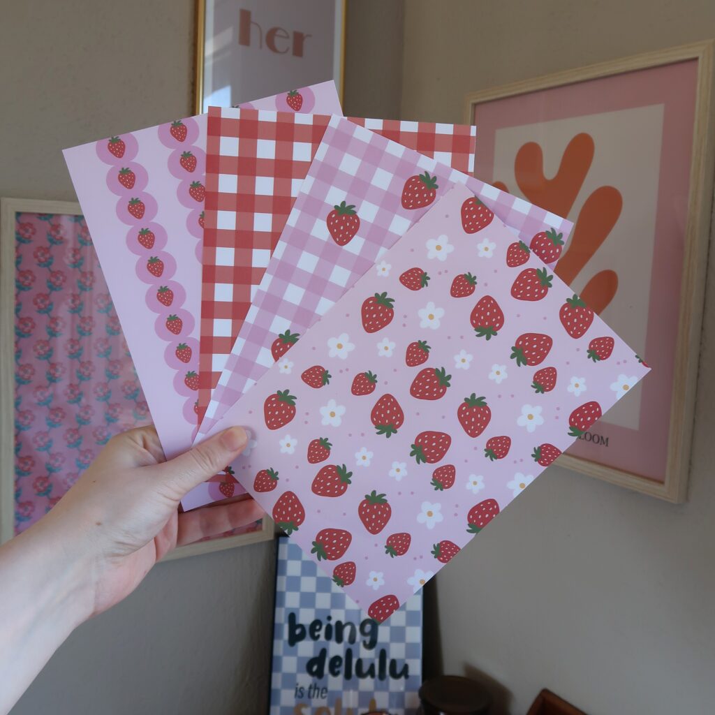 Vier vellen papier met ieder eigen patronen en illustraties met aardbeien, in rood en roze kleuren.