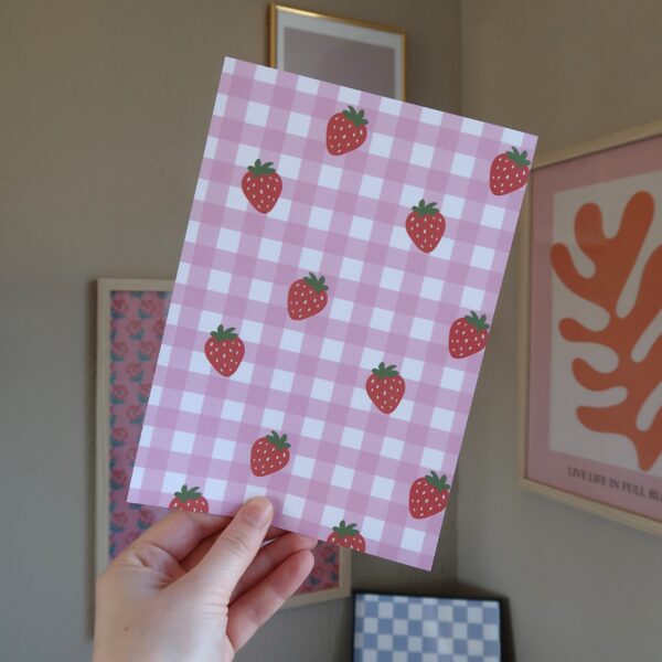 Een vel papier met een roze gingham patroon en illustraties van aardbeien, bedoelt voor het journallen of scrapbooken.