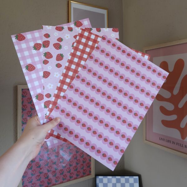 Vier vellen papier met ieder eigen patronen en illustraties met aardbeien, in rood en roze kleuren.