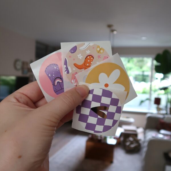 Setje met vier ronde stickers met ieder een eigen design: een roze sticker met een cowboy laars, een gele sticker met een witte bloem, een sticker met meerdere cowboy laarzen en een lila geblokte sticker met een gouden hart.