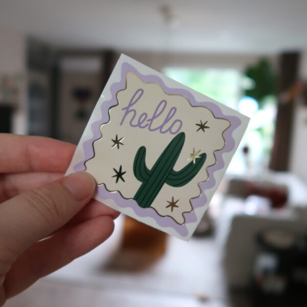 Vierkante sticker met lila, gouden details, een cactus en de tekst hello