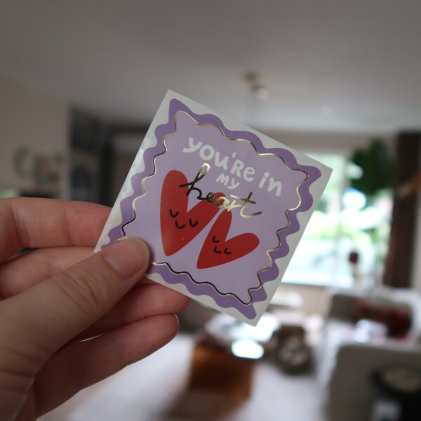 Lila vierkante sticker met twee hartjes en de tekst 'you're in my heart' en gouden details