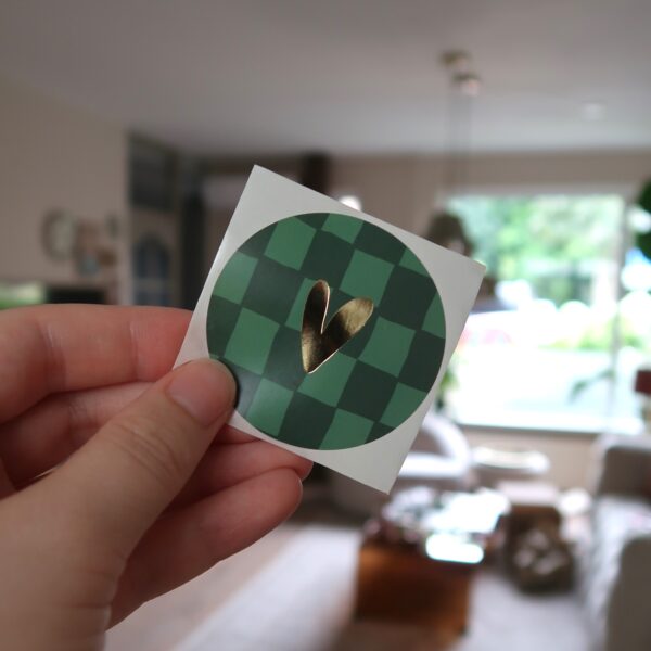 Ronde sticker met groen geblokt grid achtergrond en een gouden hartje.