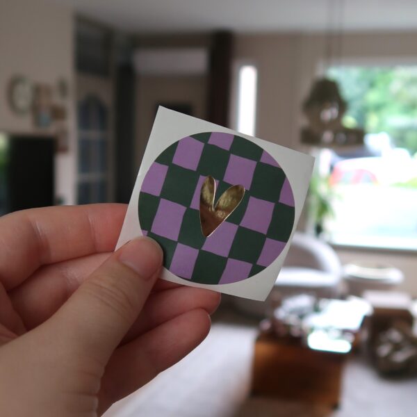 Ronde sticker met groen en lila geblokt grid achtergrond en een gouden hartje.