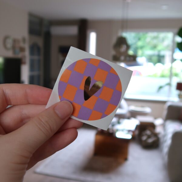 Ronde sticker met oranje en lila geblokt grid achtergrond en een gouden hartje.