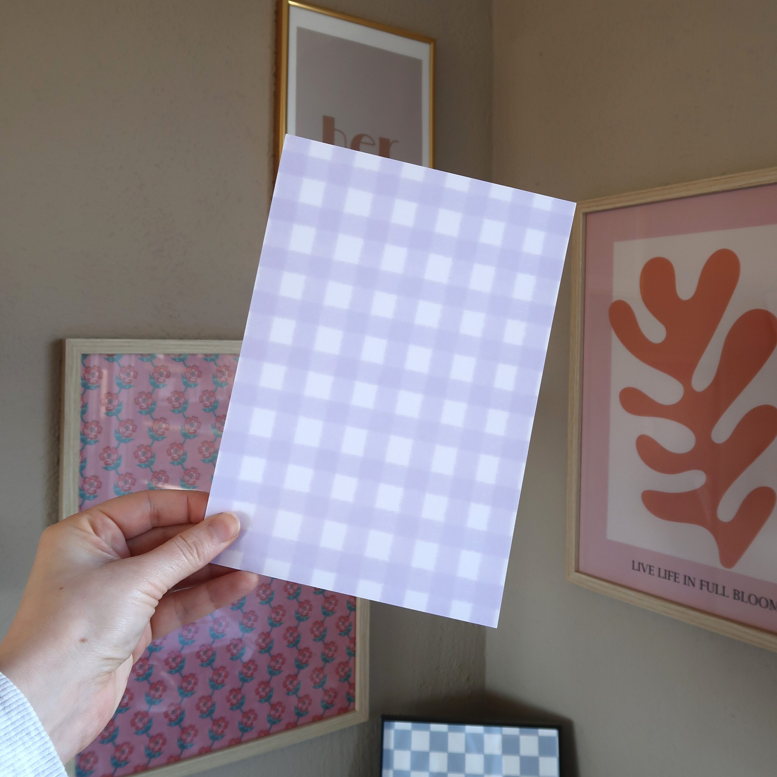 Hand die een vel papier vast houdt met een lila gingham patroon.