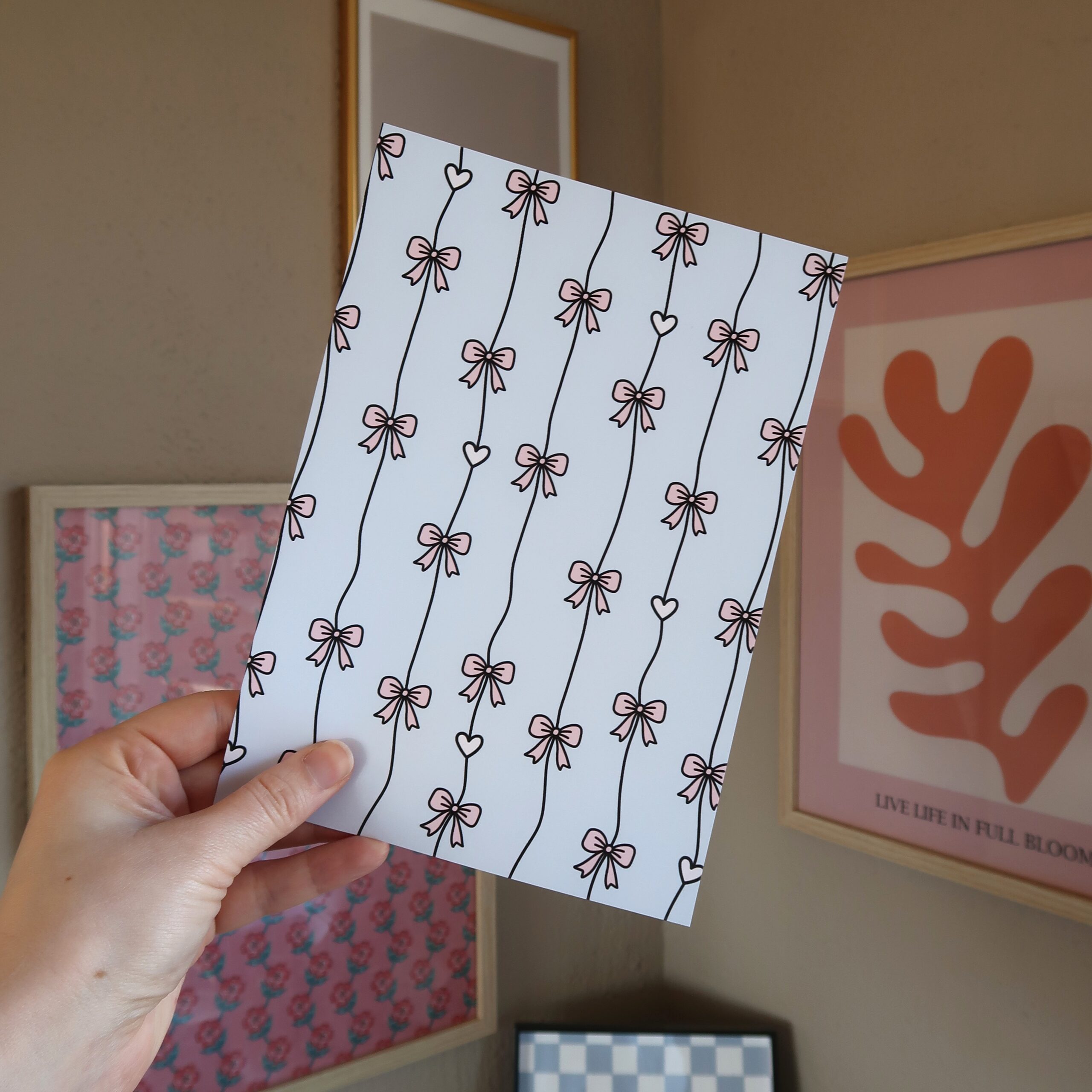 Een hand die een vel papier vast houdt met illustraties van strikjes en hartjes in pastel tinten.