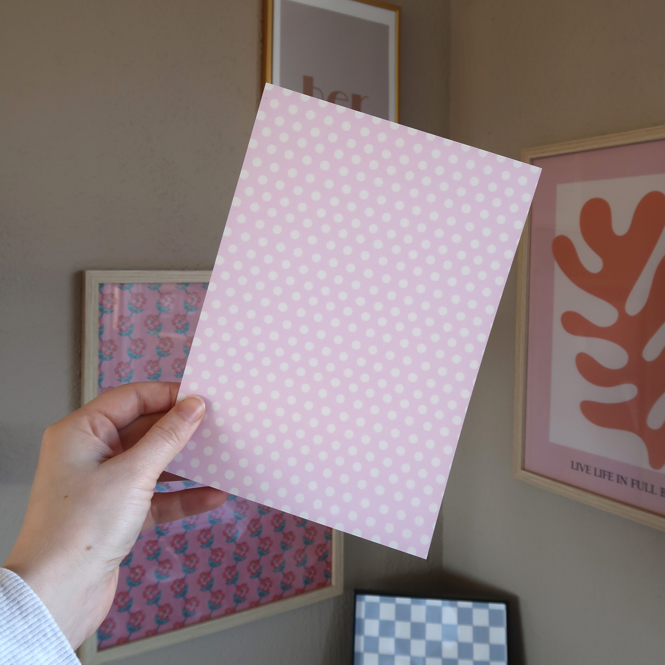 Een hand die een vel papier vast houdt in het lichtroze met witte stippen.