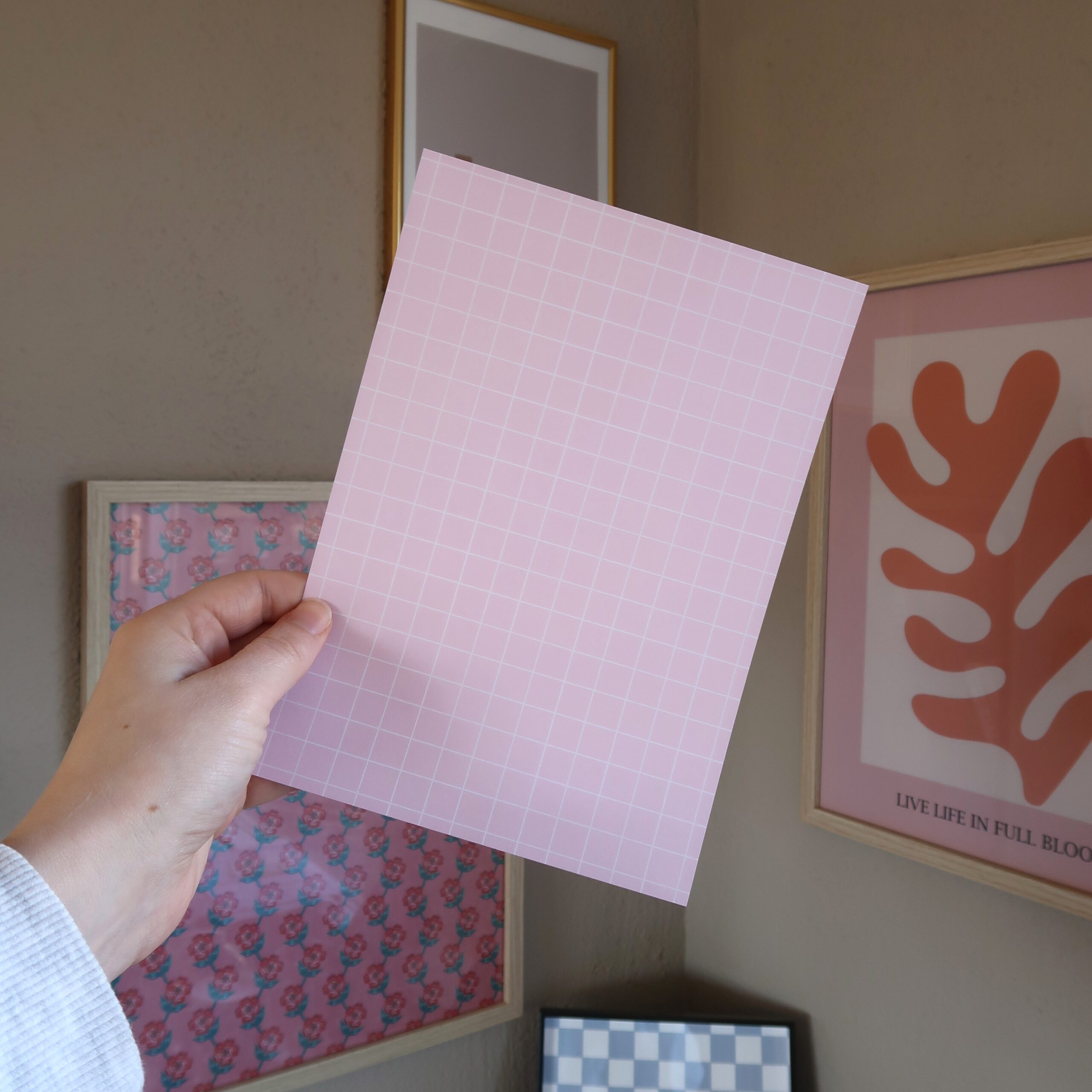Een hand die een vel papier vast houdt in het lichtroze met een witte ruit.
