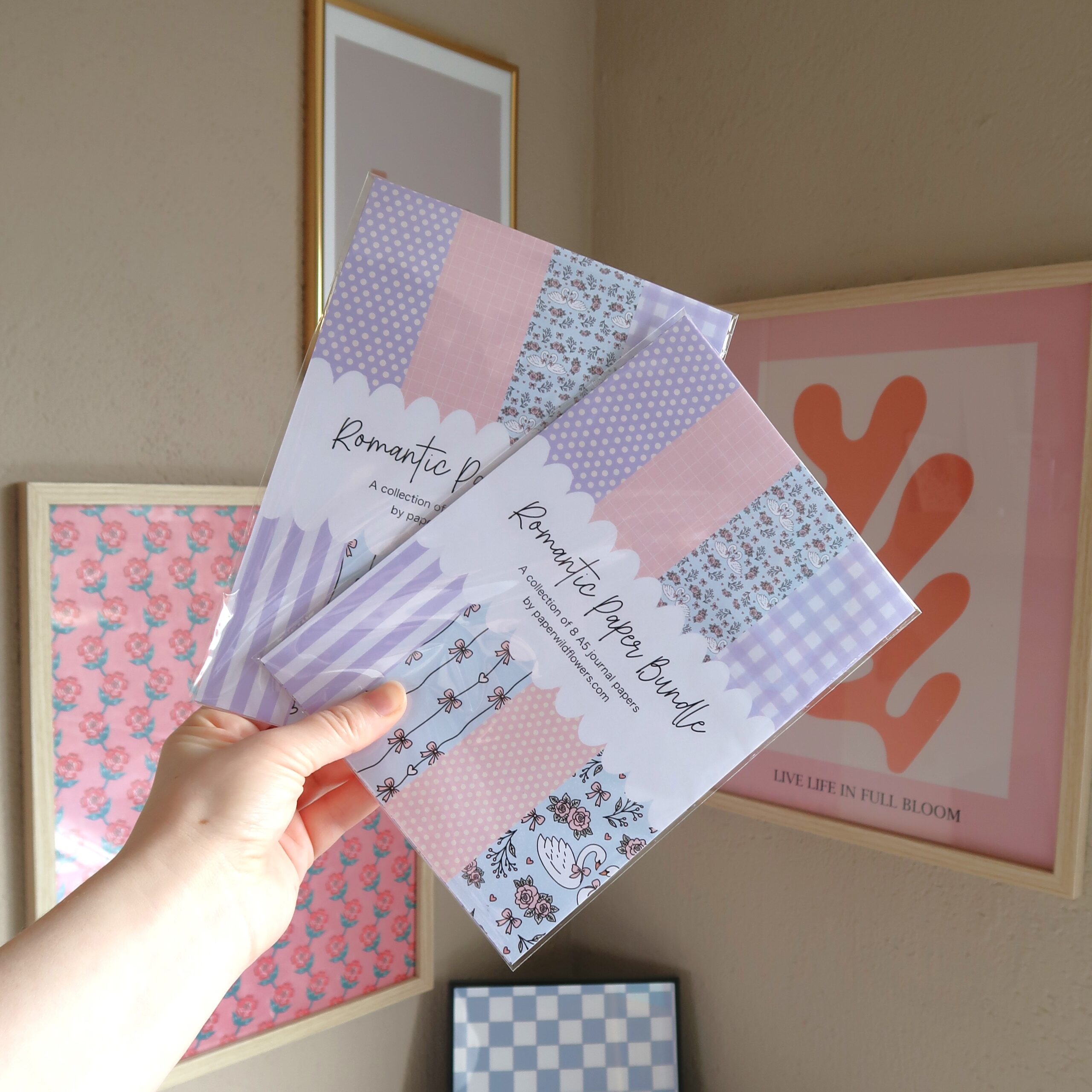 Een hand die een papier bundel met 8 vellen geïllustreerd papier vast houdt in pastel tinten en met romantische illustraties met zwanen, hartjes, rozen en strikjes.